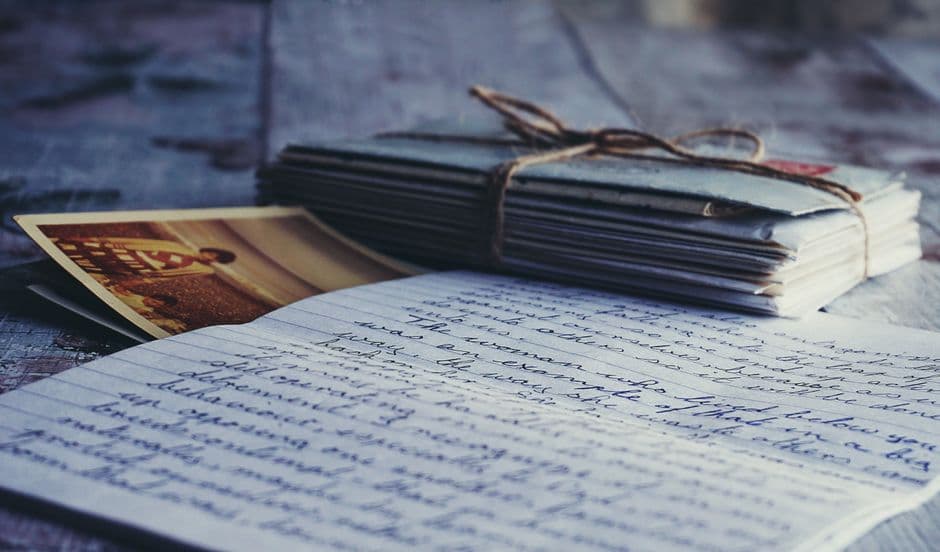A handwritten journal beside a tied bundle of old letters and a faded photograph, the kind of paper research a family historian keeps.